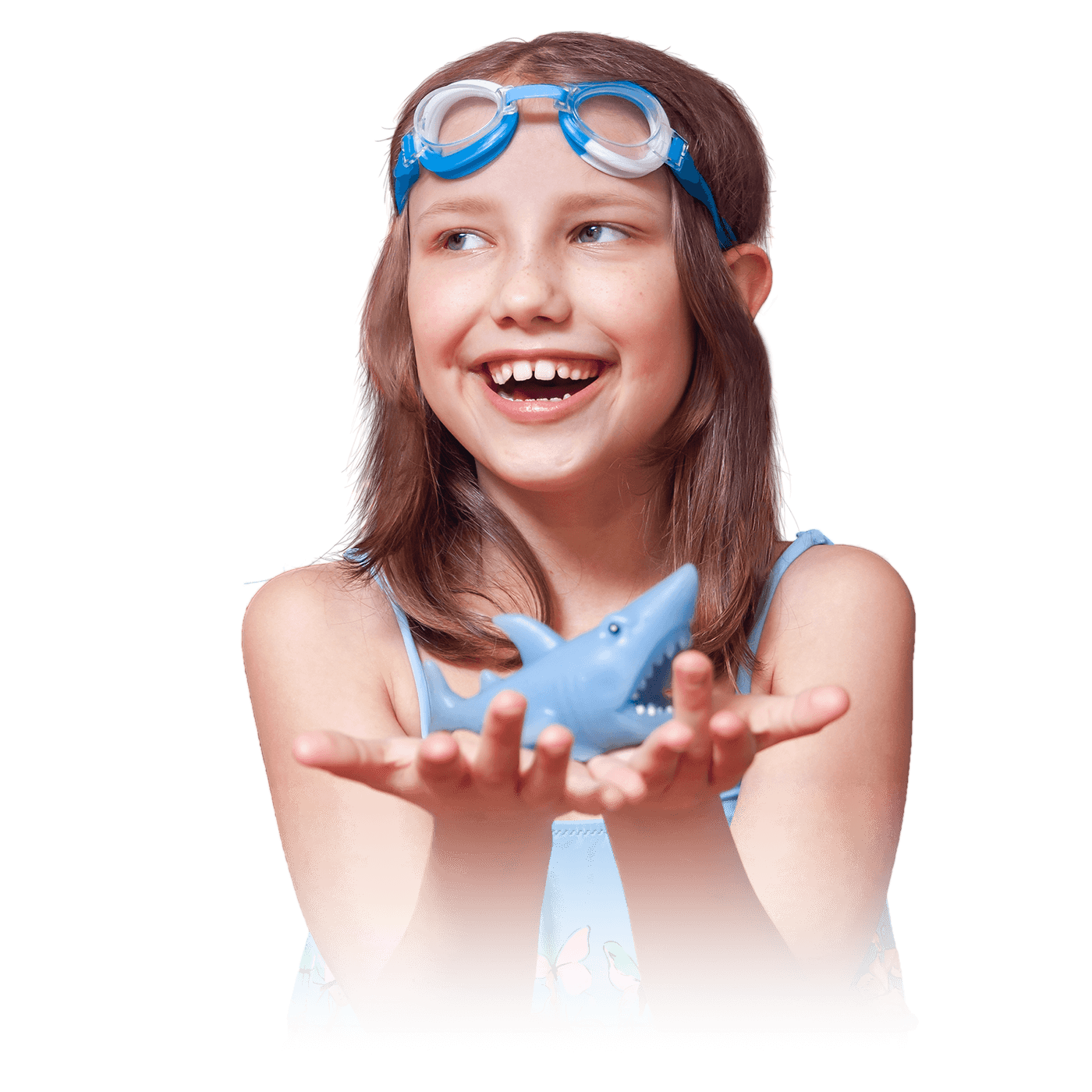 A young girl smiling with swim goggles on her forehead, holding a toy shark in her hand.